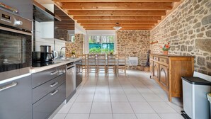 A modern kitchen with a stone wall, wooden ceiling beams, and a view of greenery outside.