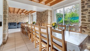 A dining area with wooden chairs and a table, stone walls, and a view of greenery outside.
