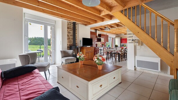 Ein großzügiger Wohnbereich mit einer Holztreppe, einer Couch, einem Couchtisch und Blick ins Freie.