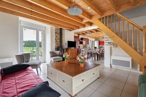 Un'ampia zona giorno con scala in legno, un divano, un tavolino da caffè e vista sull'esterno.
