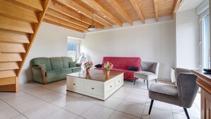 Ein geräumiges Wohnzimmer mit hoher Holzbalkendecke, einem weißen Couchtisch, einem roten Sofa, einem grünen Sofa und einem grauen Sessel.