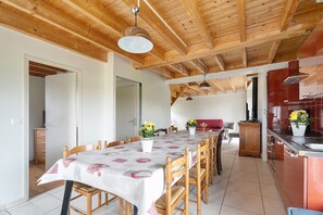 Zona pranzo con soffitto in legno, tavolo con sedie, angolo cottura con pensili rossi e un corridoio.