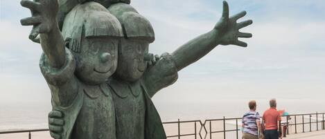 Eine bronzene Statue von zwei Kindern mit ausgestreckten Armen, die auf einen Strand blickt.