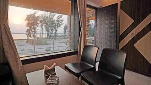 A room with a large window, two black chairs, a small table, and a view of trees and water outside. - HYAT LUXURY (Mandarmani)