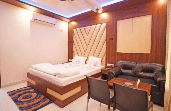 A modern hotel room with a wooden headboard bed, a black leather sofa, a small dining table, and a blue and orange rug. - HYAT LUXURY (Mandarmani)