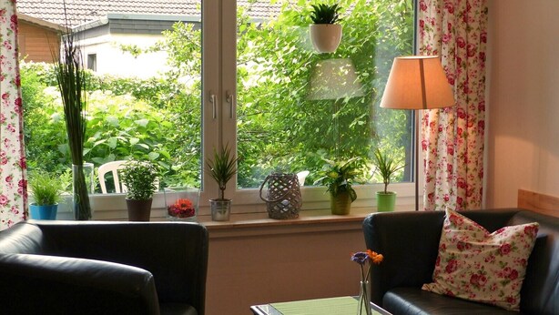 Een woonkamer met een zwarte leren bank, een bijzettafeltje en een raam met uitzicht op groen.