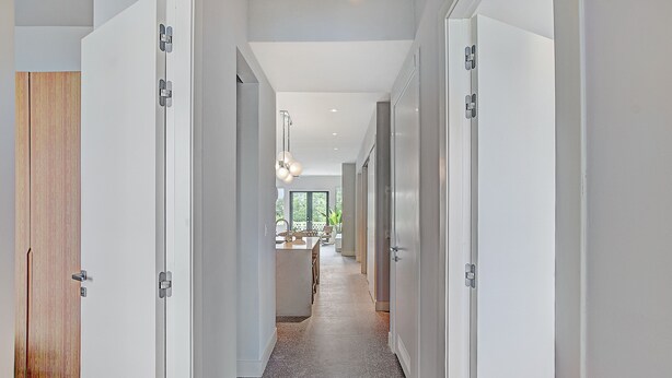 Un pasillo moderno con puertas blancas, una puerta de madera y una zona de cocina al fondo.