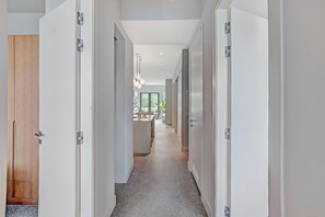 Un corridoio moderno con porte bianche, una porta in legno e una zona cucina in lontananza.