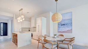 Una cocina moderna con armarios blancos, una isla central y un comedor con sillas de madera y una mesa de mármol.