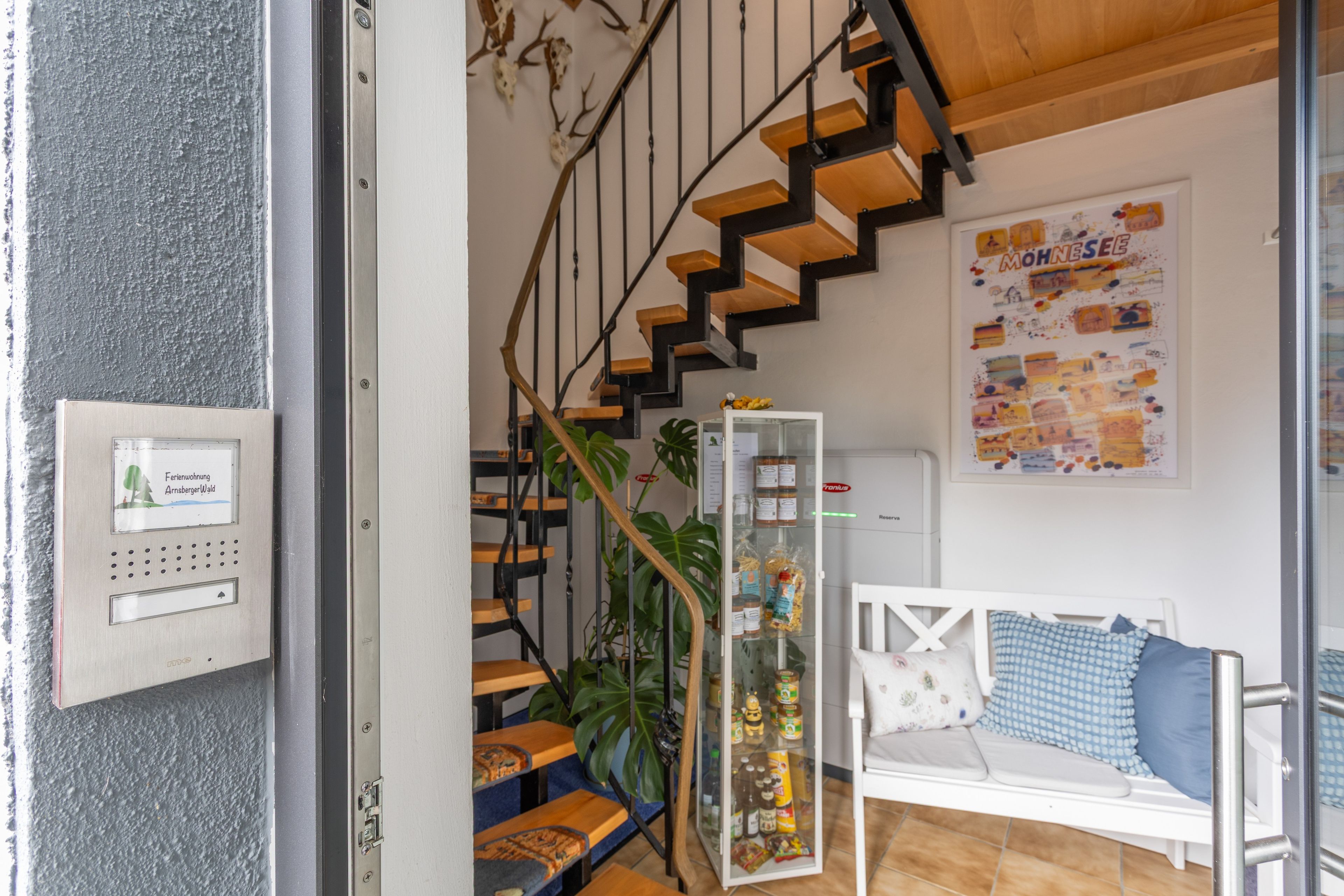 Eine Treppe mit Holzstufen und Metallgeländern, ein weißes Sofa mit gemusterten Kissen und eine Vitrine mit Lebensmitteln.