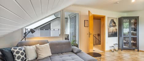 Ein modernes Wohnzimmer mit einem grauen Ecksofa, einem Couchtisch und einer Fernbedienung.