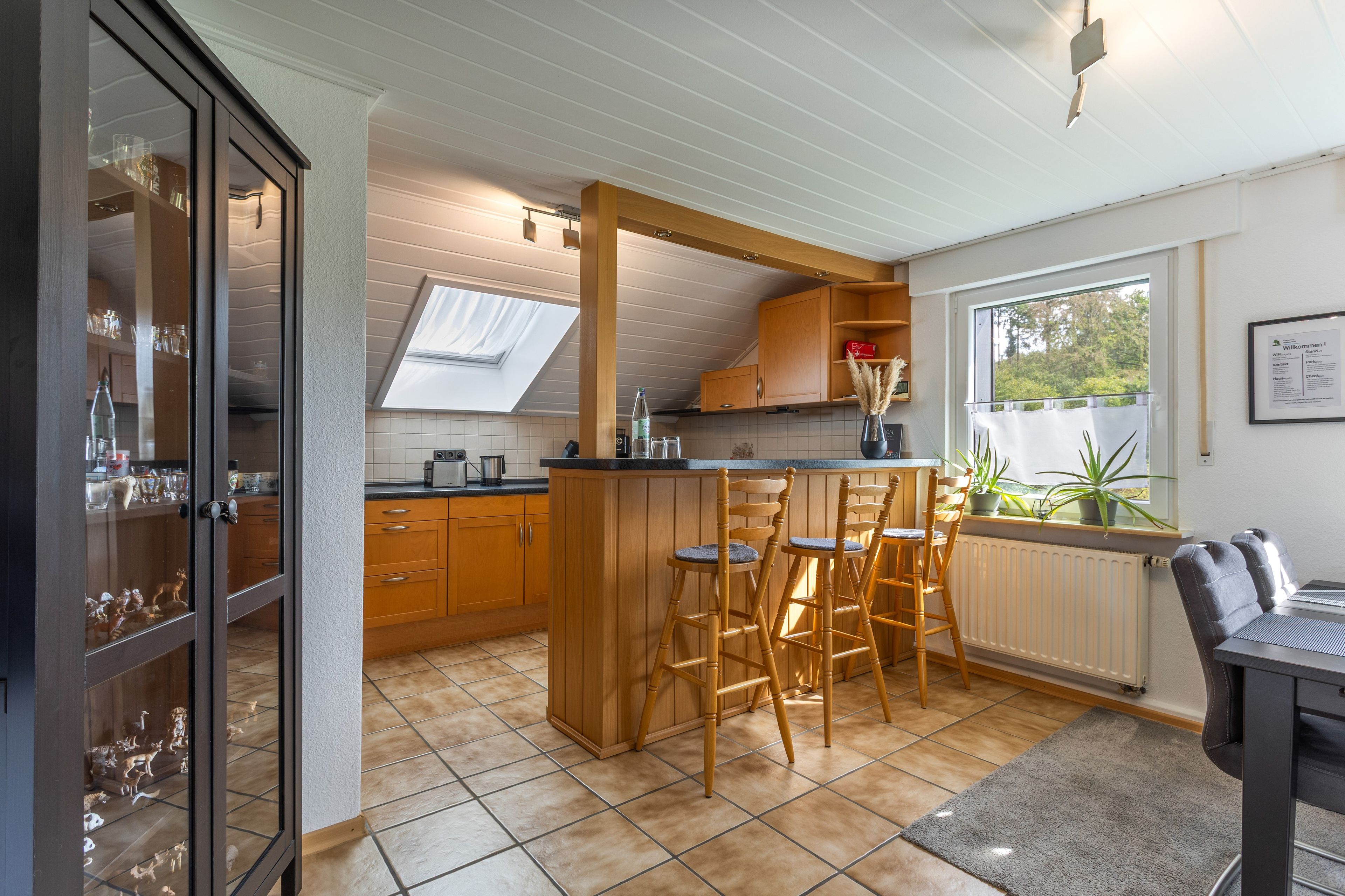 Eine Küche mit Holzausstattung, einer Bar mit Hockern, einem Oberlicht und einem Fenster mit Pflanzen.