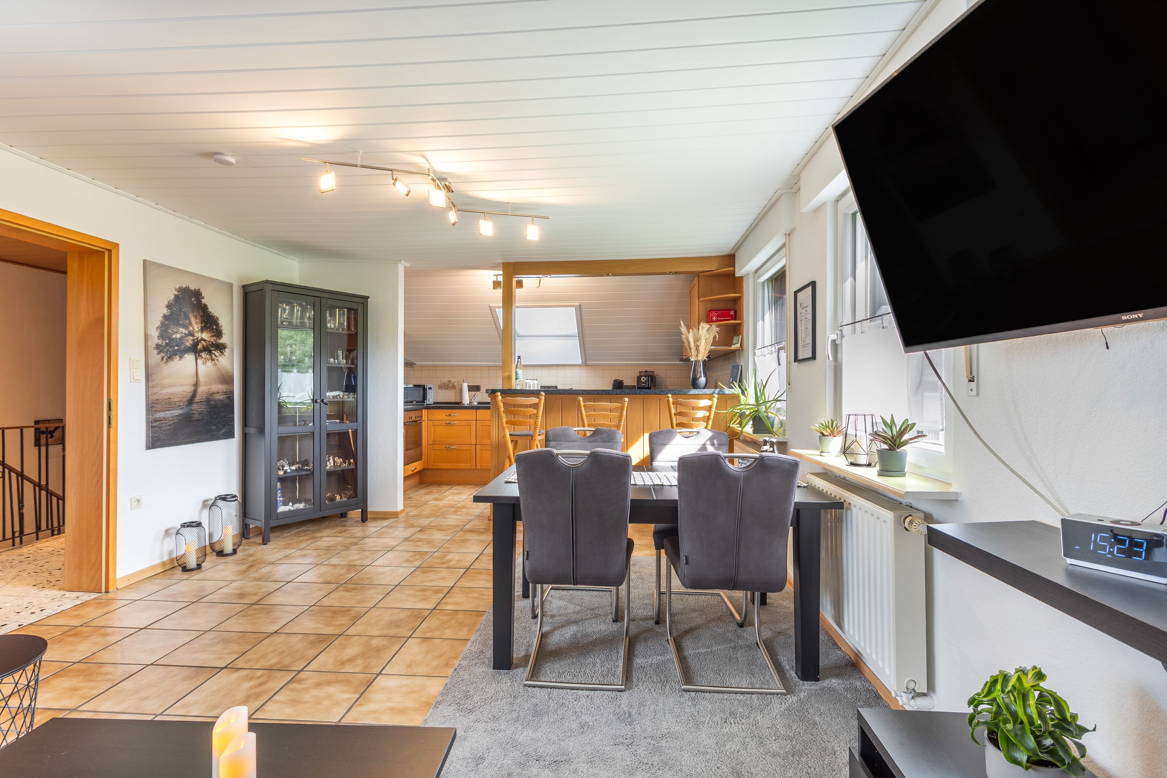 Eine moderne Küche mit Essbereich, einem flachbildfernseher an der Wand und Blick in den angrenzenden Wohnraum.