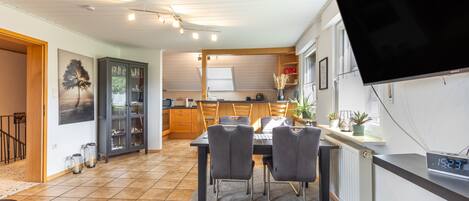 Une cuisine moderne avec un coin repas, un téléviseur à écran plat fixé au mur et une vue sur l’espace de vie adjacent.