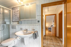 Ein Badezimmer mit Toilette, Waschbecken und Dusche. An der Wand befindet sich ein Schild mit deutschem Text.