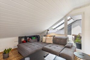 Un salon moderne avec un canapé d’angle, une table basse, une bibliothèque et une plante en pot.
