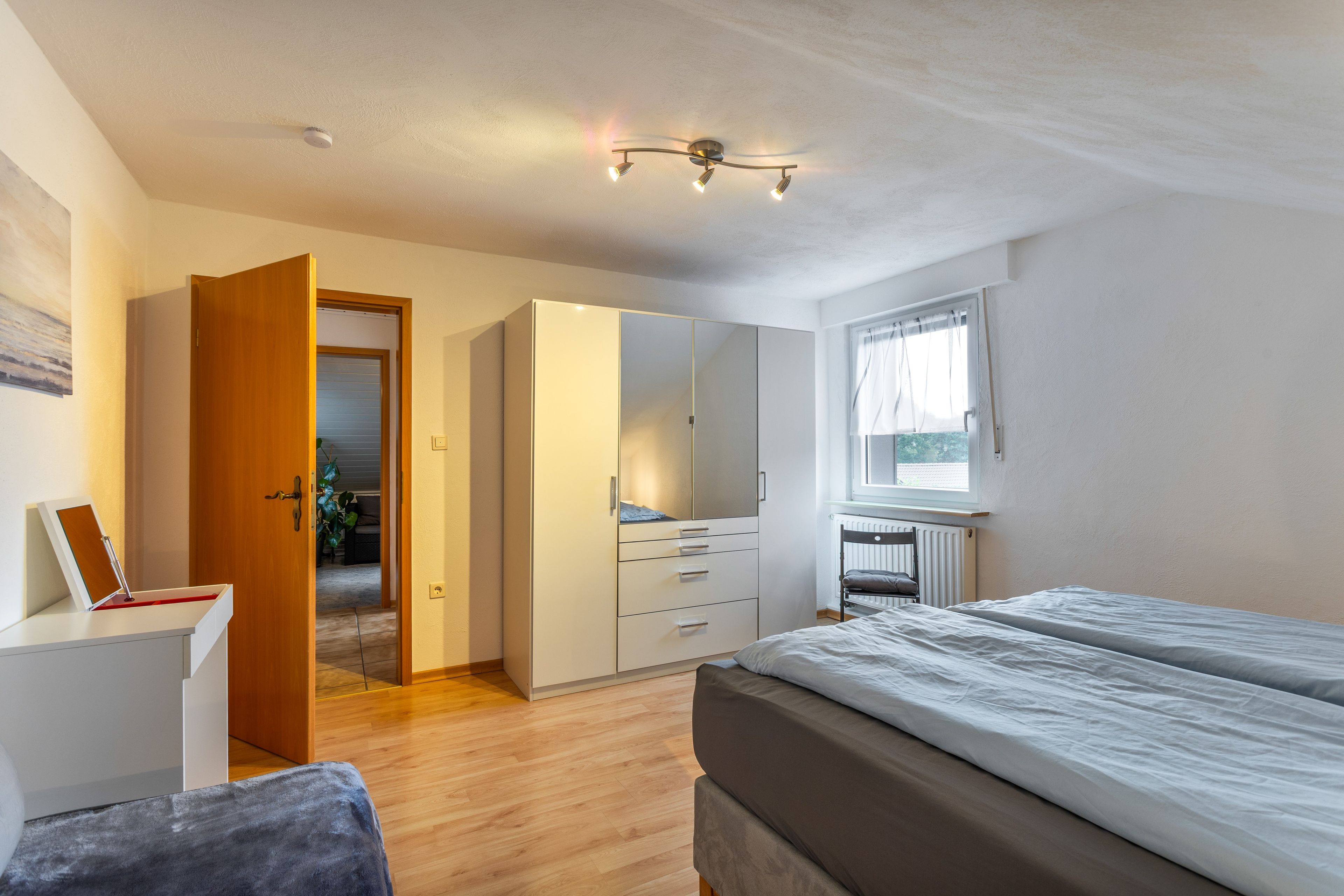 Ein Schlafzimmer mit Bett, Schreibtisch, Kleiderschrank und Fenster.
