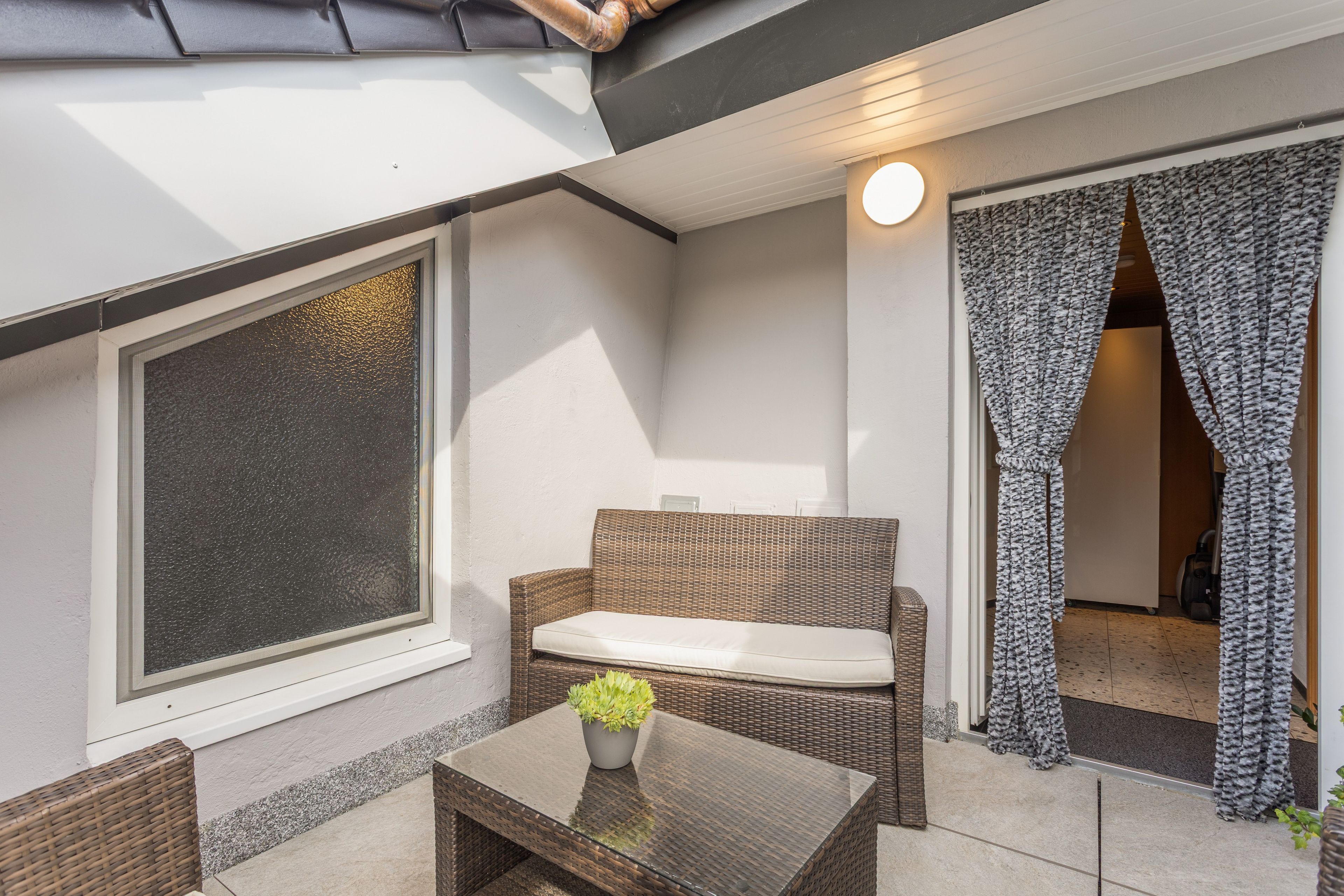 A balcony with a wicker sofa, a glass table, and a potted plant.
