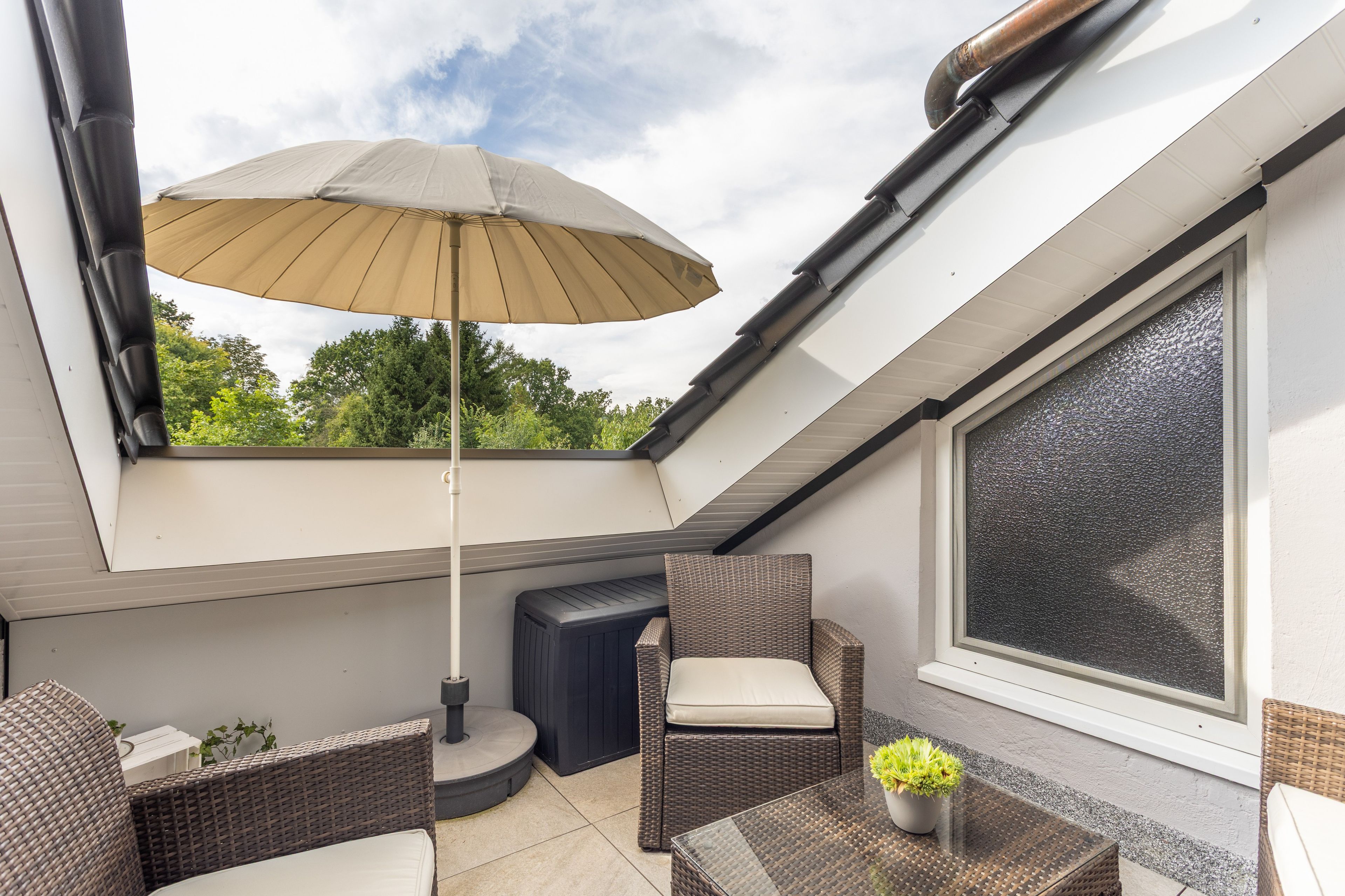 A rooftop terrace with a table, chairs, an umbrella, and a potted plant.
