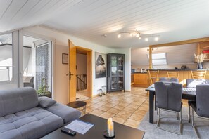 Ein modernes Wohnzimmer mit einem grauen Sofa, ein Essbereich mit Tisch und Stühlen, eine Küche mit Holzschränken und ein Flur, der zu einer Treppe führt.