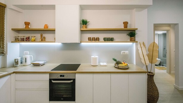 Een moderne keuken met witte kasten, houten aanrecht en inbouwplanken. Op het aanrecht staat een koffiezetapparaat, een waterkoker en een fruitmand.