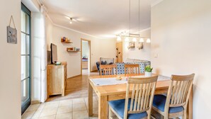 A dining area with a wooden table and chairs, a kitchen in the background, and a view through a window. - Apartment "64 sqm" with Private Terrace, Shared Garden, and Wi-Fi (Olsberg)