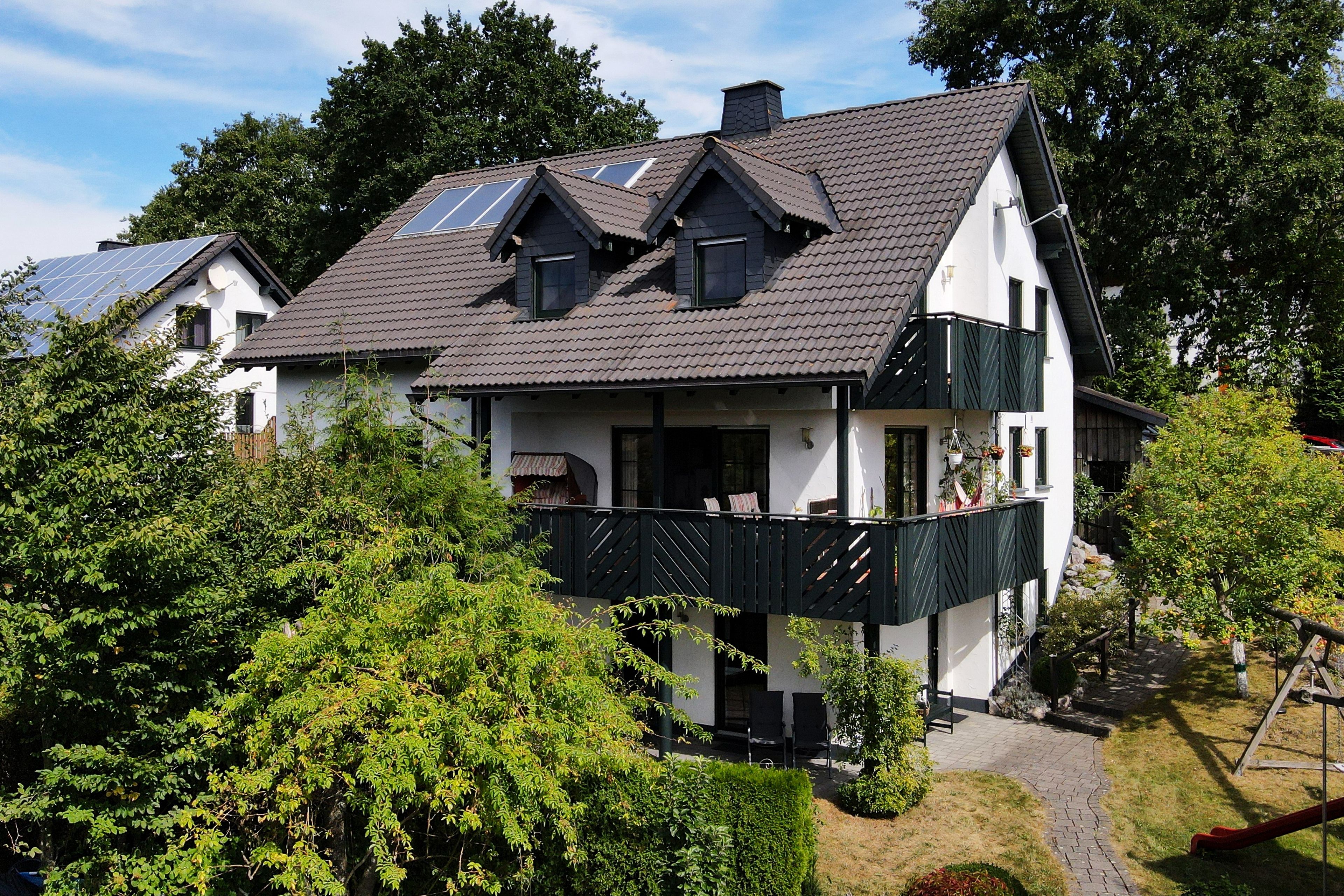 A two-story house with a balcony, solar panels, and a garden.