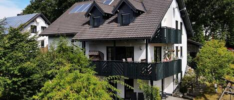 A two-story house with a balcony, solar panels, and a garden.