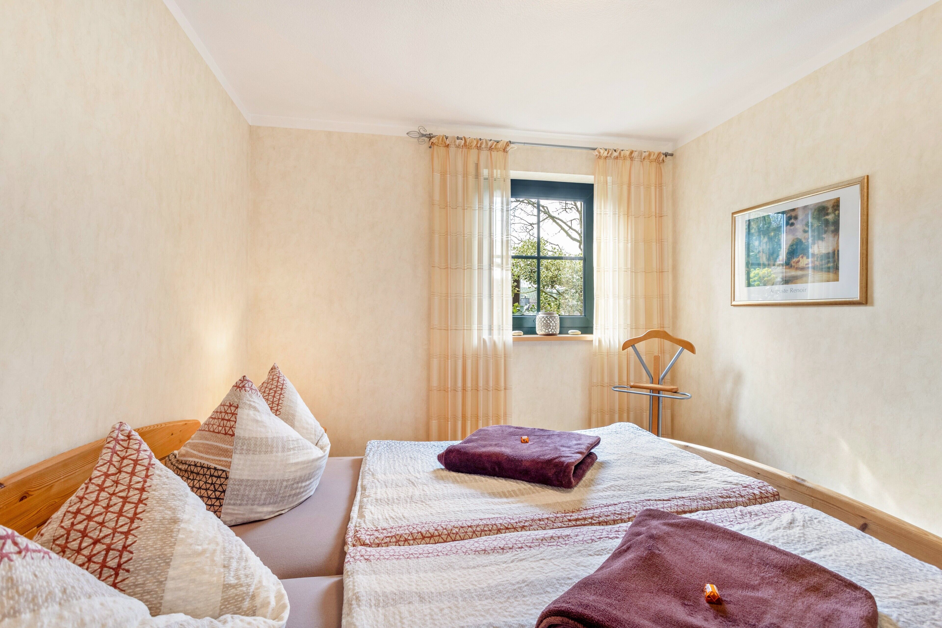 Ein Zimmer mit zwei Betten, einem Vorhangfenster, einem Sessel und einem gerahmten Bild an der Wand.