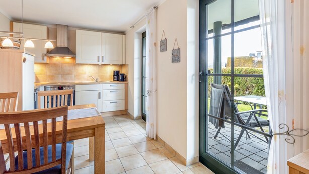 A kitchen with white cabinets, a dining table with chairs, and a view through a glass door to an outdoor area. - Apartment "64 sqm" with Private Terrace, Shared Garden, and Wi-Fi (Olsberg)