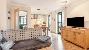A living room with a sofa, a TV, wooden cabinets, and a kitchen in the background. - Apartment "64 sqm" with Private Terrace, Shared Garden, and Wi-Fi (Olsberg)