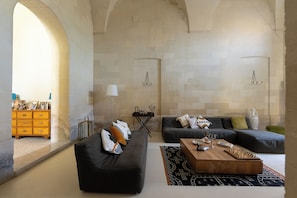 A modern living room with a dark sofa, a wooden coffee table, and a patterned rug. There is a fireplace with a mantel and a small side table. - Garden Apartment - Palazzo Villani Lubelli (Cannole)