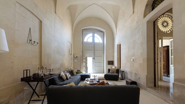 Amplia sala de estar con un sofá negro grande, una mesa de centro y una mesita auxiliar con objetos decorativos. Un arco de entrada da a otra habitación.
