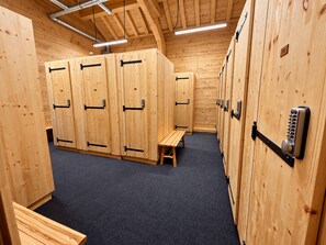 A row of wooden lockers with metal handles and a bench in a locker room with a dark carpet.