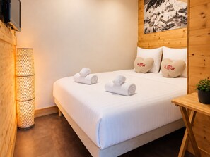 Ein Hotelzimmer mit einem Bett, zwei herzförmigen Kissen, einem aufgerollten weißen Handtuch, einem an der Wand befestigten Fernseher und einer Stehlampe.