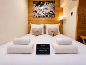 A hotel room with a wooden headboard, two heart-shaped pillows, a bed with white linens, and a sign in French.
