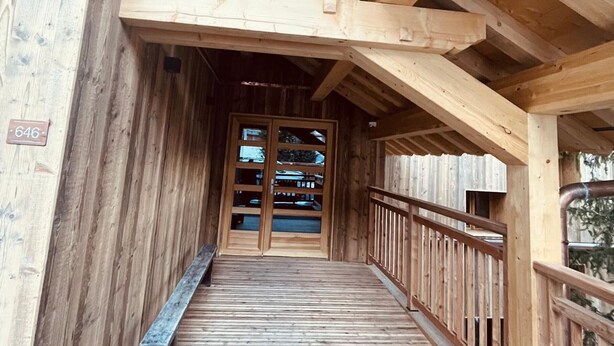 Un porche cubierto de madera con una escalera de madera que da a una puerta de cristal.