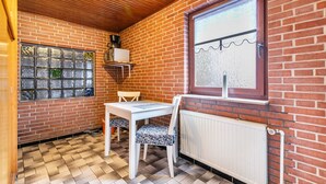 Um quarto pequeno com parede de tijolos, janela com vista, radiador e mesa com cadeiras.