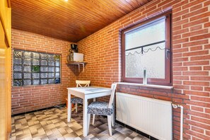 A small room with a brick wall, a window with a view, a radiator, and a table with chairs. - Beautiful Fitter's Apartment 6 in Weddingstedt, Schleswig-Holstein (Weddingstedt ot Weddinghusen)