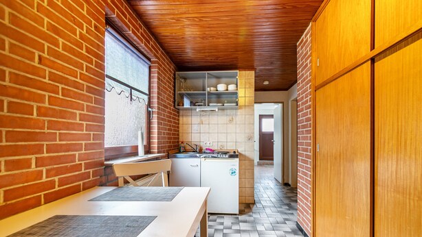 Uma cozinha pequena com parede de tijolos, armários de madeira, uma geladeira compacta e piso de azulejos.