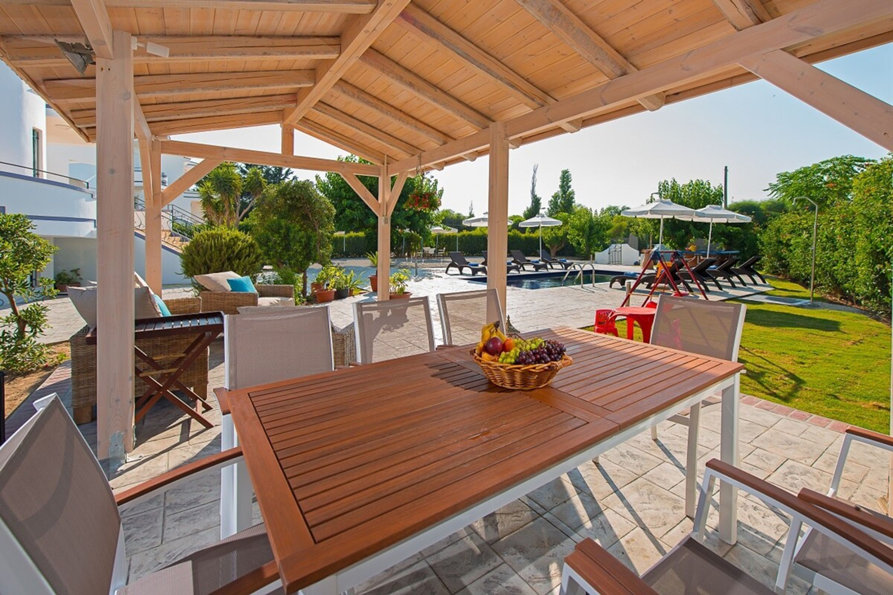 An outdoor patio with a wooden table, chairs, and a fruit basket.