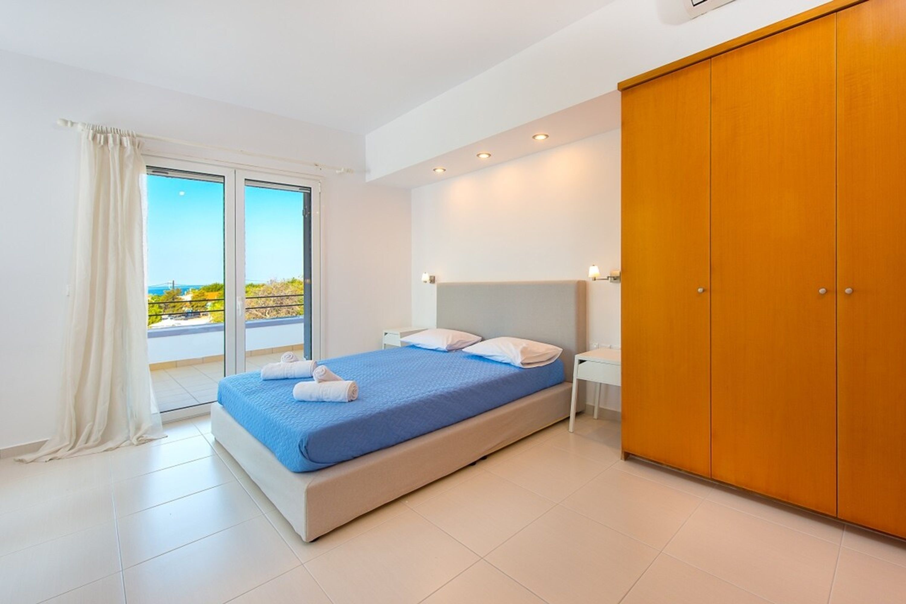 A bedroom with a bed, a wardrobe, a nightstand, and a view through a window.