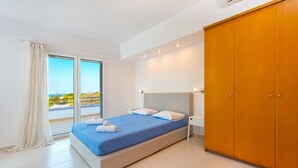 Ein Schlafzimmer mit Bett, Schrank, Nachttisch und Blick durch ein Fenster.