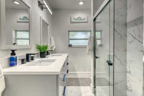 Ein modernes Badezimmer mit zwei Waschbecken, einer Duschkabine aus Glas und einer Topfpflanze.