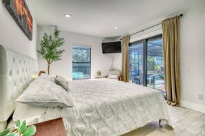 A bedroom with a large bed, a plant, a TV, and a view of the outdoors. - Venice 3BR Canal Home | Heated Pool, Near Braves (Venice)