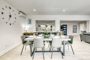 A modern dining area with a clock on the wall, a central island with a plant, and a kitchen in the background. - Venice 3BR Canal Home | Heated Pool, Near Braves (Venice)