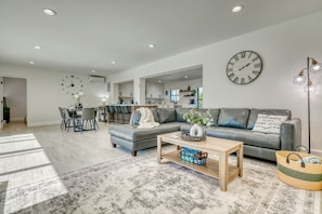 A modern living room with a grey sofa, a coffee table, and a dining area with chairs. - Venice 3BR Canal Home | Heated Pool, Near Braves (Venice)