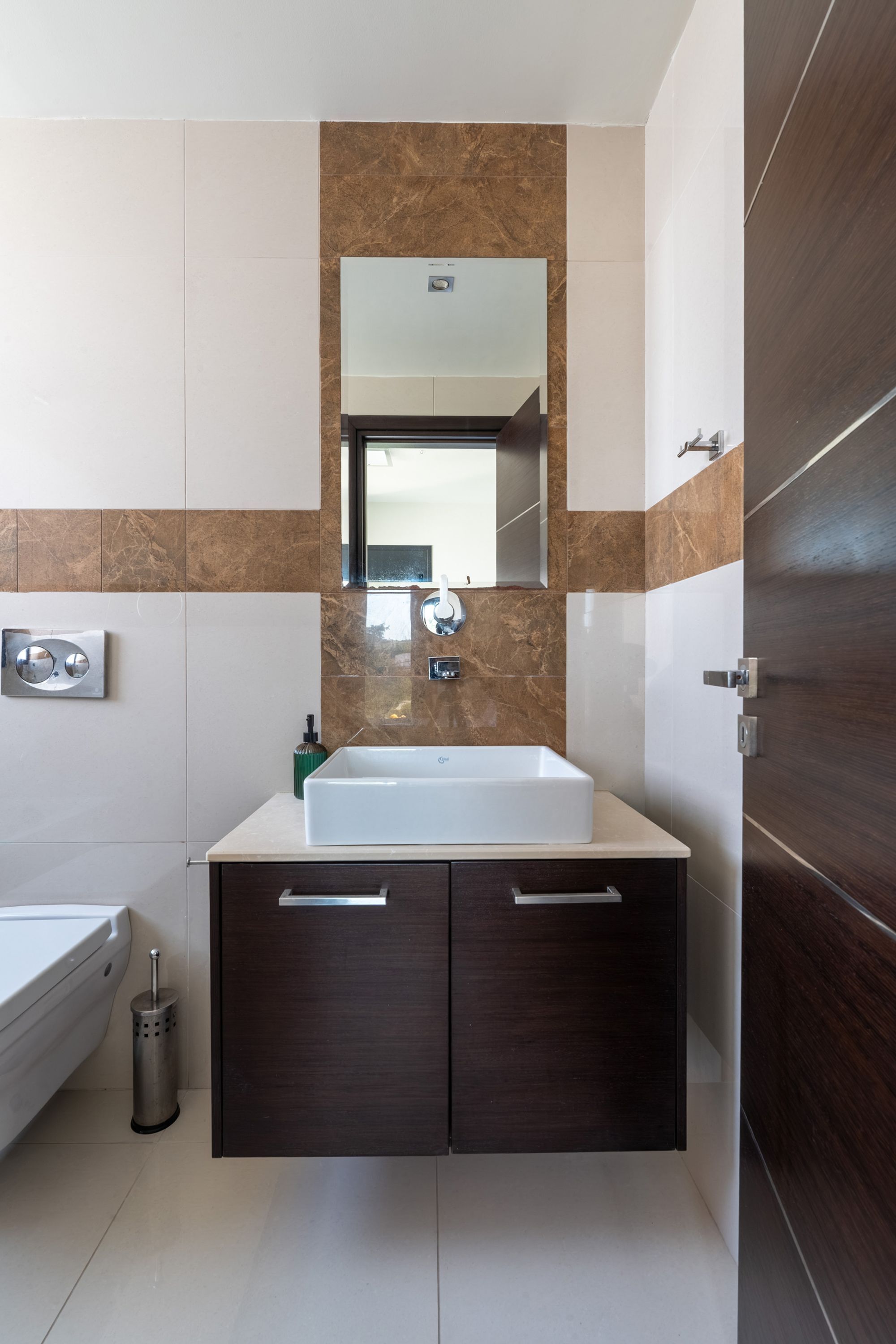 Een moderne badkamer met een witte wastafel, donkere houten kastjes, een spiegel en een toilet.
