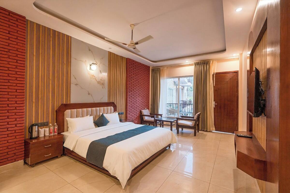 A hotel room with a large bed, a desk with chairs, a TV, and a balcony with curtains.