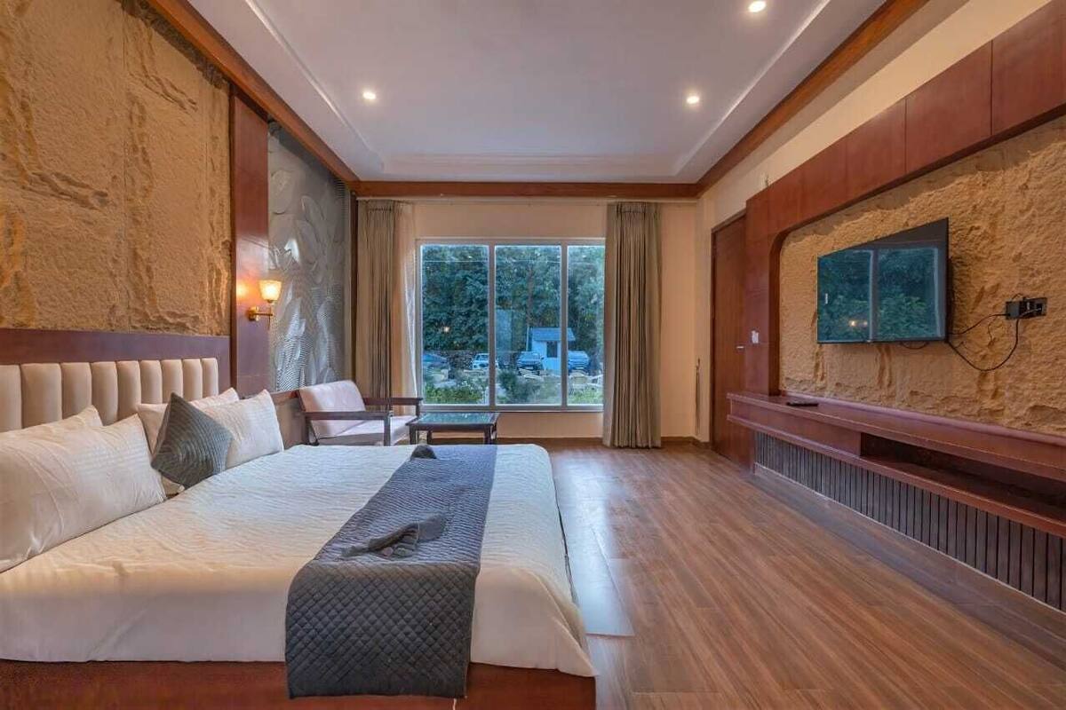 A hotel room with a large bed, a television mounted on the wall, and a view of the outdoors through a large window.
